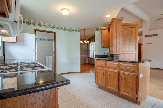 kitchen with white appliances, a sink, a chandelier, light tile patterned flooring, and a peninsula
