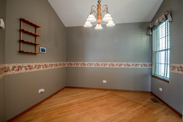 spare room with a chandelier, healthy amount of natural light, wood finished floors, lofted ceiling, and baseboards