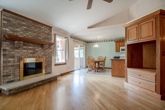 living room featuring vaulted ceiling, a ceiling fan, a brick fireplace, light wood-type flooring, and baseboards