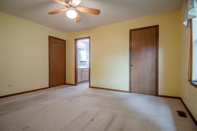 unfurnished bedroom featuring light colored carpet, baseboards, ensuite bath, and ceiling fan