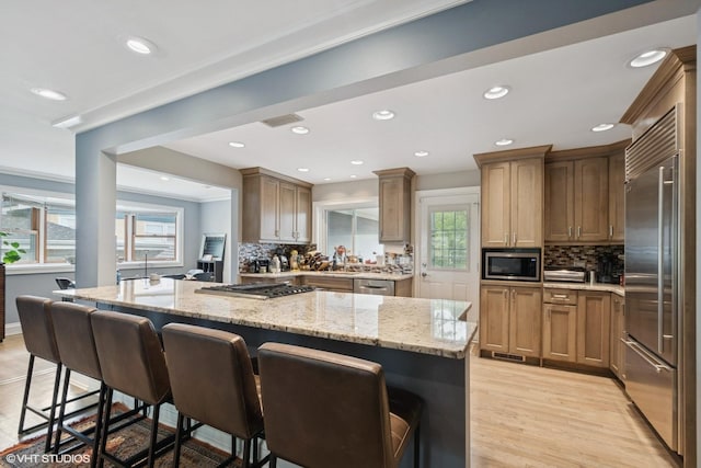 4253 Grove St, Skokie, IL 60076 - kitchen featuring appliances with stainless steel finishes, light stone counters, a kitchen breakfast bar, decorative backsplash, and recessed lighting