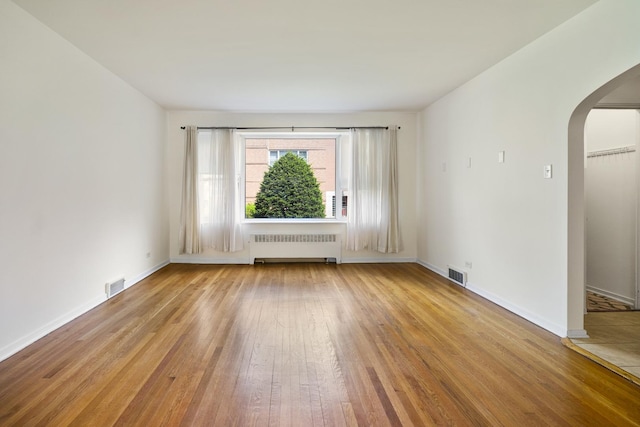 spare room featuring radiator, arched walkways, hardwood / wood-style flooring, and baseboards