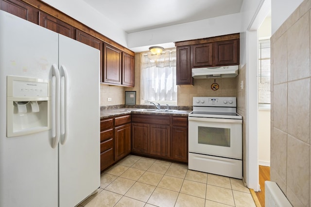kitchen featuring white appliances, under cabinet range hood, a sink, dark countertops, and tasteful backsplash