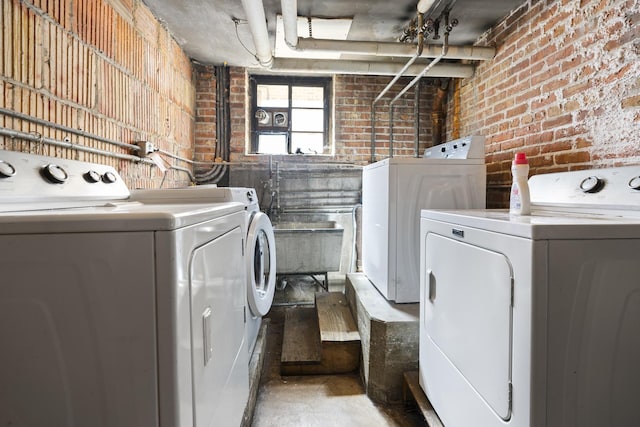 laundry area with washer and clothes dryer and brick wall