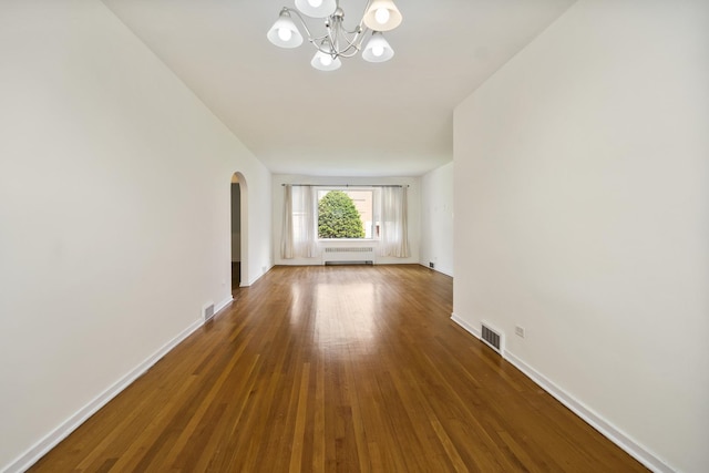 unfurnished room with radiator heating unit, arched walkways, a chandelier, and baseboards