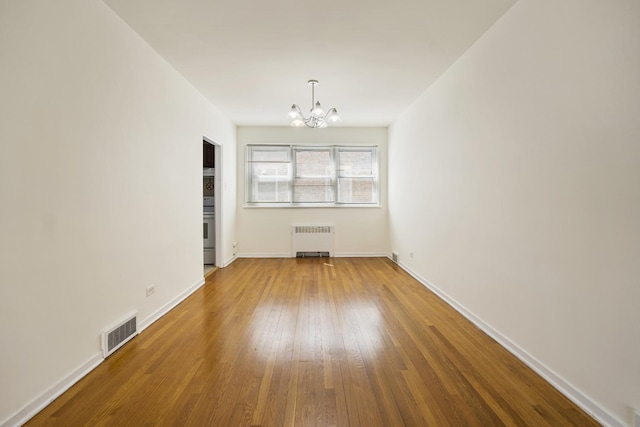 unfurnished living room with radiator heating unit, a chandelier, wood-type flooring, and baseboards