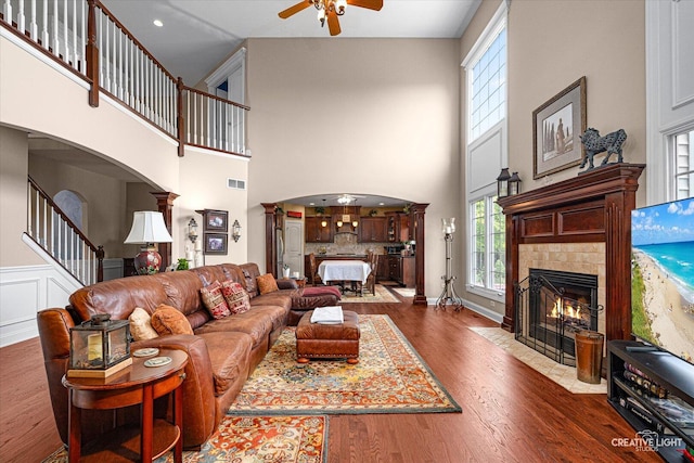 25700 Pastoral Dr, Plainfield, IL 60585 - living area with arched walkways, a ceiling fan, a tiled fireplace, a high ceiling, and dark wood-style floors