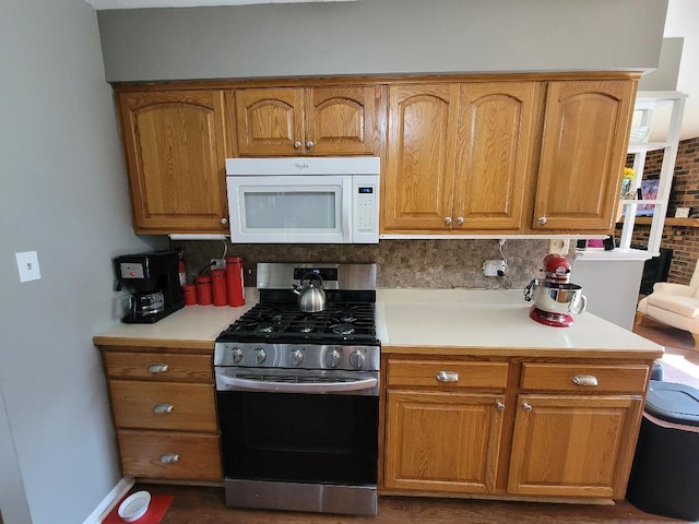 kitchen with white microwave, gas stove, light countertops, brown cabinets, and baseboards