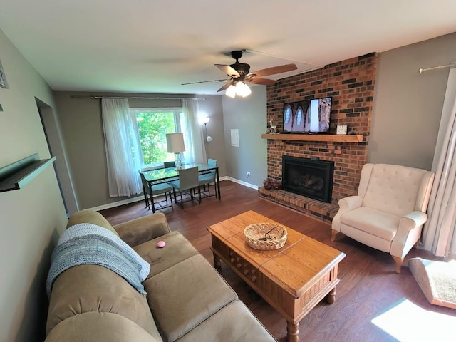 living room featuring wood finished floors, ceiling fan, a brick fireplace, and baseboards