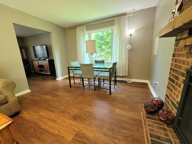 dining space featuring wood finished floors, a brick fireplace, and baseboards