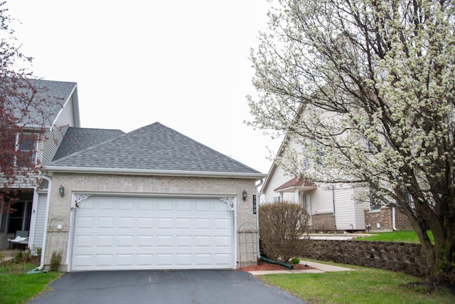 view of side of property featuring driveway, a shingled roof, a garage, and brick siding