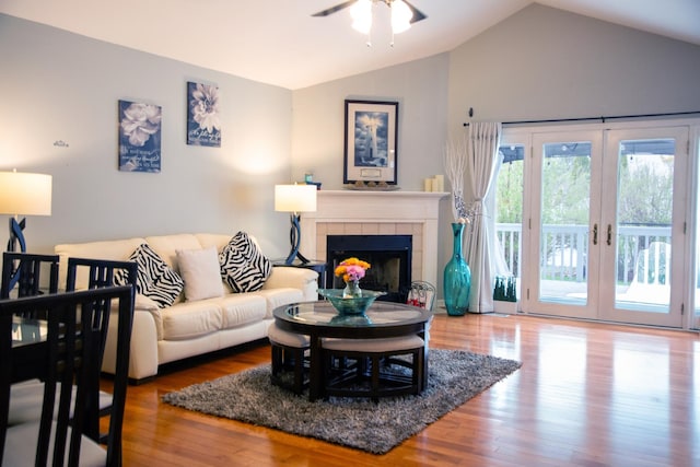 living area with lofted ceiling, ceiling fan, a tiled fireplace, and wood finished floors