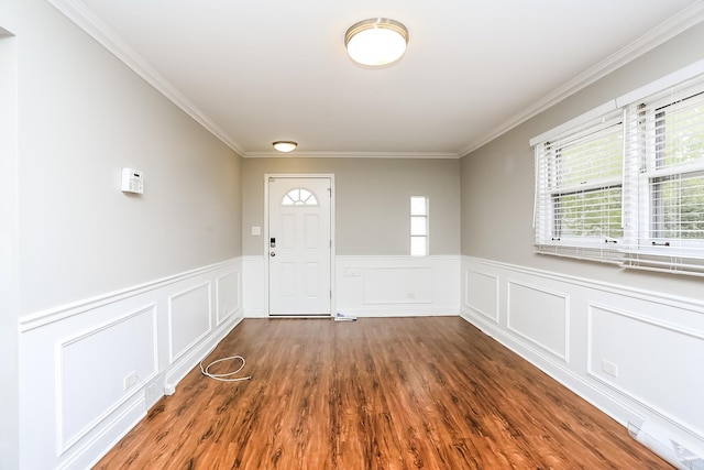 entryway featuring crown molding, plenty of natural light, wainscoting, wood finished floors, and a decorative wall