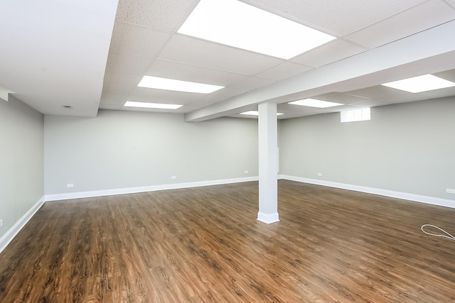 below grade area featuring dark wood finished floors, baseboards, and a drop ceiling