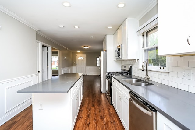 kitchen with appliances with stainless steel finishes, a sink, a kitchen island, white cabinetry, and wainscoting