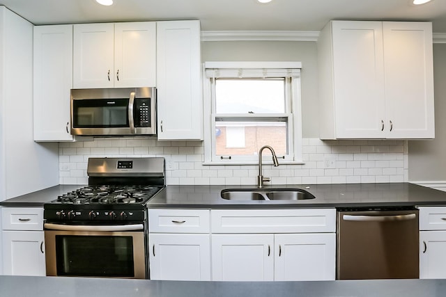 kitchen featuring appliances with stainless steel finishes, a sink, dark countertops, crown molding, and white cabinets