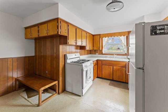 341 W Glen Flora Ave, Waukegan, IL 60085 - kitchen with white appliances, brown cabinetry, a sink, light countertops, and wooden walls