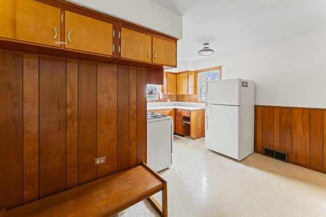 341 W Glen Flora Ave, Waukegan, IL 60085 - kitchen featuring white appliances, brown cabinets, a wainscoted wall, wooden walls, and light countertops