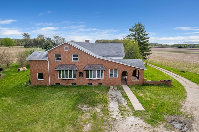 view of front of house featuring brick siding, a front lawn, dirt driveway, and roof with shingles