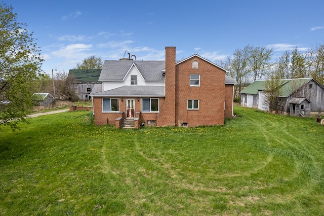 rear view of house featuring brick siding, a chimney, a yard, and a detached garage