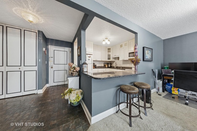 10 E Ontario St Unit 1303, Chicago, IL 60611 - kitchen with a textured ceiling, a kitchen breakfast bar, glass insert cabinets, baseboards, and dark stone countertops