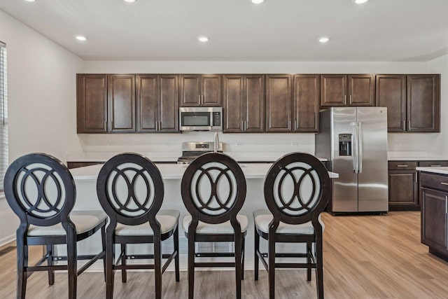 1486 Keller St, Elburn, IL 60119 - kitchen with appliances with stainless steel finishes, light countertops, a kitchen island with sink, dark brown cabinets, and light wood-style flooring