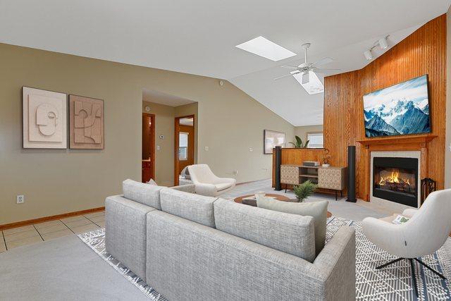 1622 Evergreen Ave, Crown Point, IN 46307 - living room with a ceiling fan, lofted ceiling, a skylight, a fireplace with flush hearth, and light tile patterned flooring