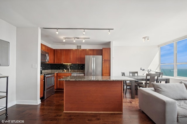 kitchen with appliances with stainless steel finishes, dark wood finished floors, backsplash, dark stone countertops, and open floor plan