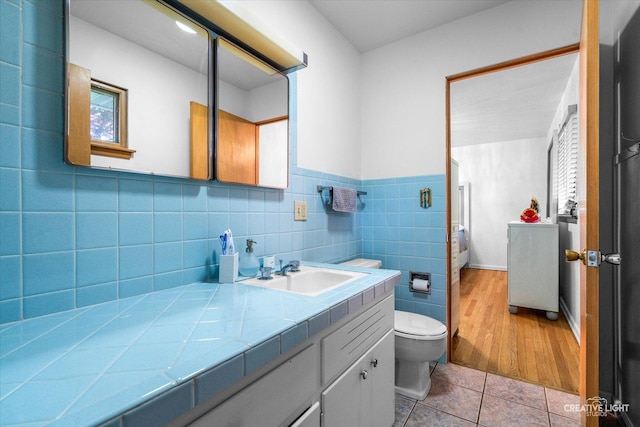 bathroom featuring tile patterned flooring, vanity, tile walls, toilet, and wainscoting