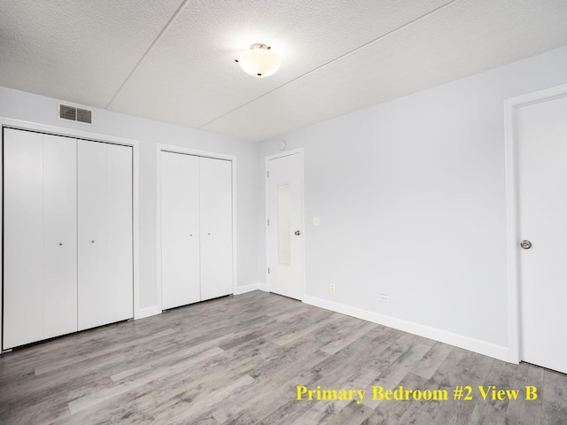 8540 W Foster Ave Unit 403, Norridge, IL 60706 - unfurnished bedroom featuring two closets, wood finished floors, baseboards, and a textured ceiling