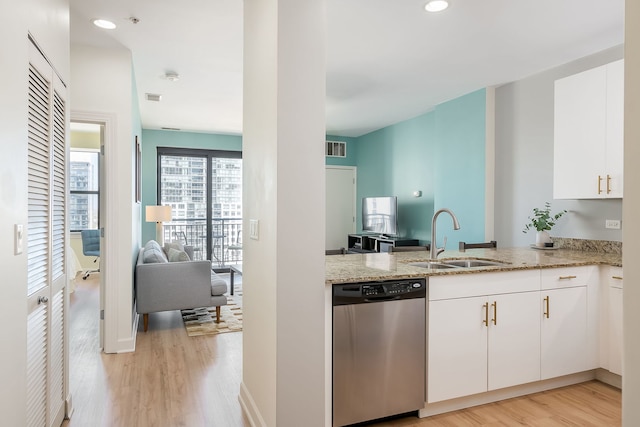 kitchen with stainless steel dishwasher, a sink, light wood-style floors, light stone counters, and white cabinetry