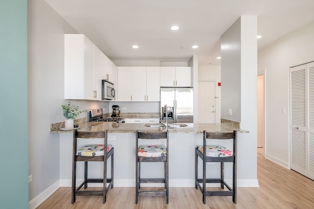 kitchen featuring appliances with stainless steel finishes, a peninsula, light wood finished floors, light stone countertops, and recessed lighting