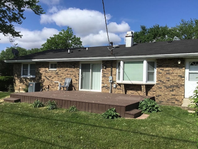 back of property featuring brick siding, a wooden deck, a chimney, and a lawn