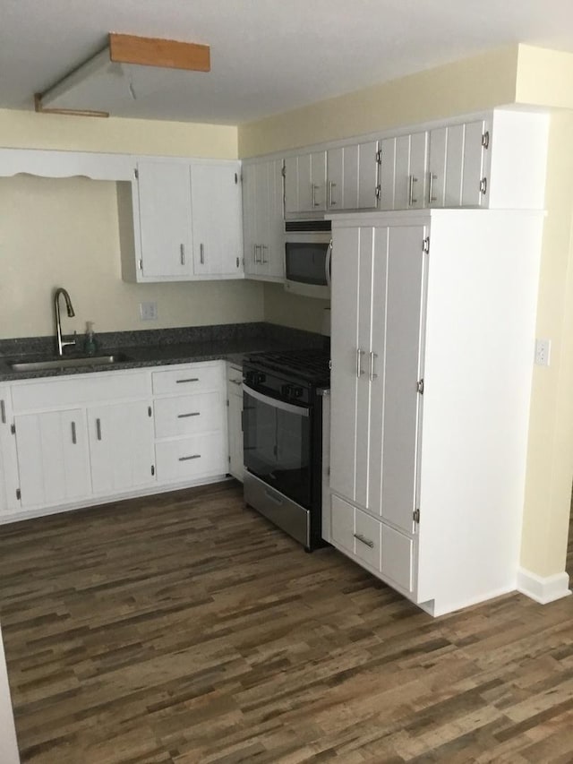 kitchen featuring gas range, a sink, stainless steel microwave, dark countertops, and dark wood finished floors