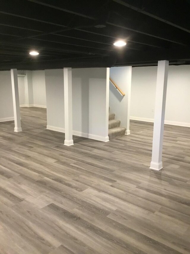 finished below grade area featuring baseboards, wood finished floors, and stairway