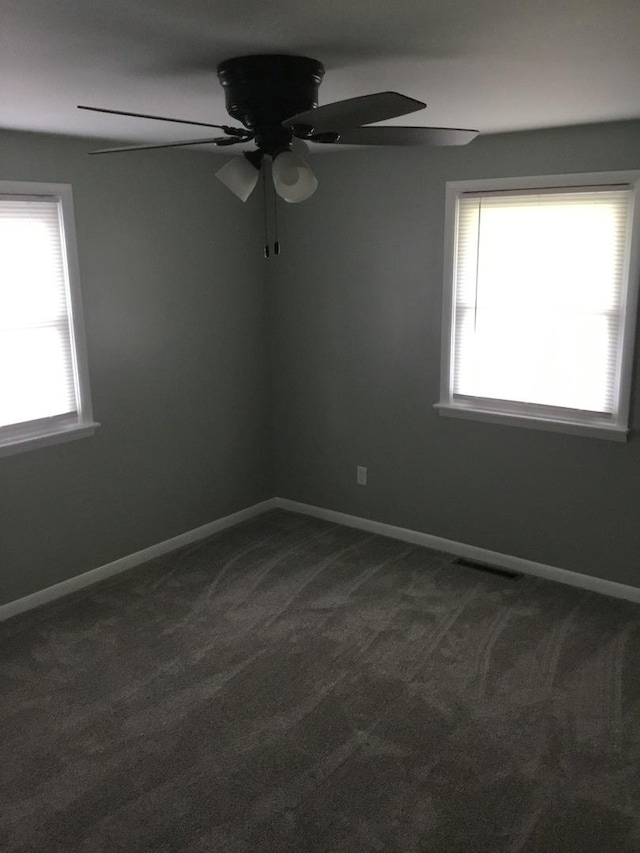 empty room featuring healthy amount of natural light, a ceiling fan, dark carpet, and baseboards
