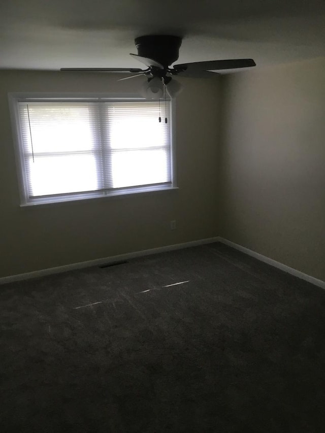 unfurnished room with a ceiling fan, baseboards, and dark colored carpet