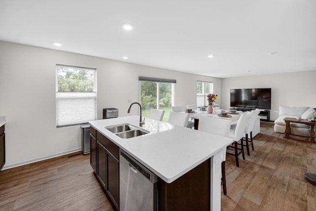 kitchen featuring a sink, stainless steel dishwasher, light wood finished floors, light countertops, and an island with sink