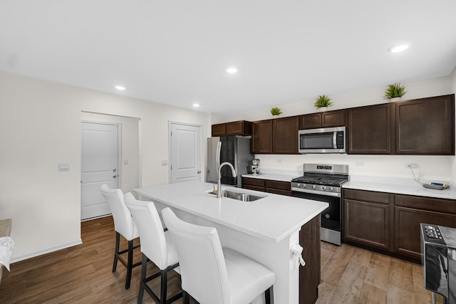 kitchen with appliances with stainless steel finishes, a sink, a kitchen bar, an island with sink, and light wood finished floors