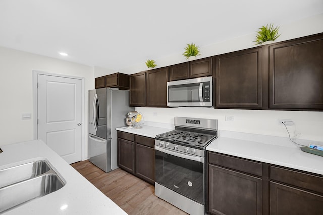 kitchen featuring appliances with stainless steel finishes, light wood finished floors, light countertops, a sink, and dark brown cabinets