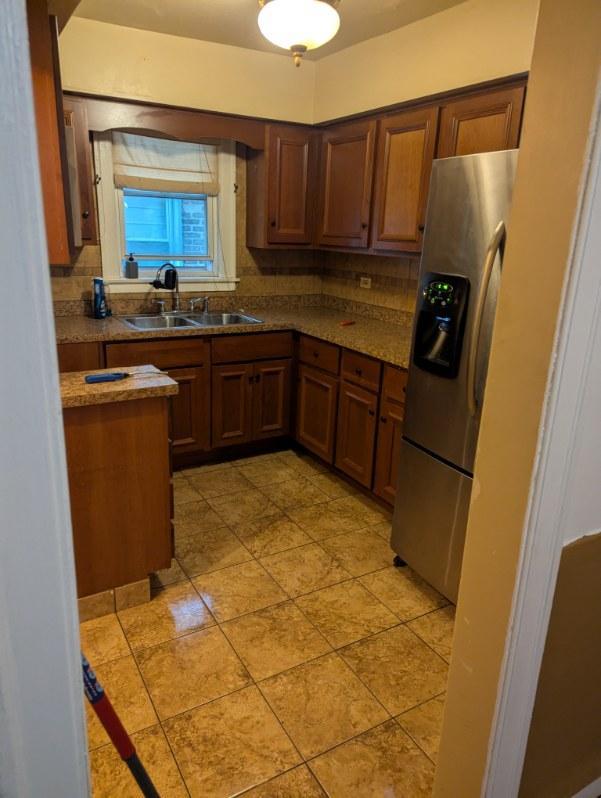 10421 S Prairie Ave, Chicago, IL 60628 - kitchen featuring stainless steel fridge with ice dispenser, a sink, light tile patterned floors, and brown cabinetry