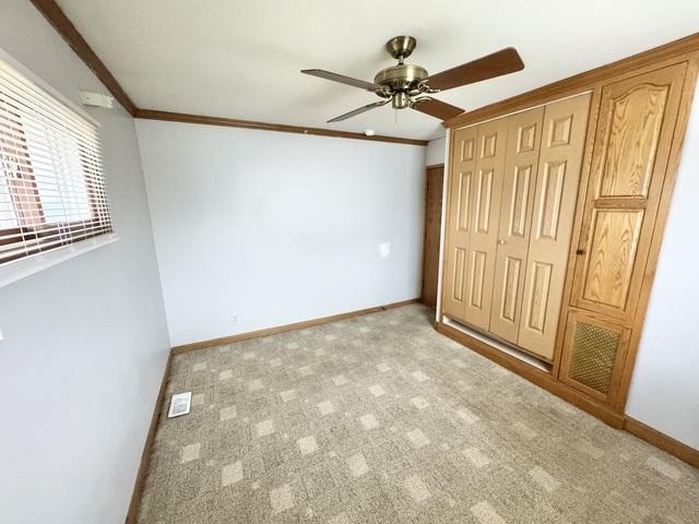 unfurnished bedroom featuring a closet, crown molding, baseboards, light carpet, and ceiling fan
