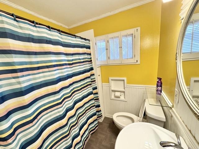 full bathroom with a wainscoted wall, toilet, crown molding, and a shower with shower curtain