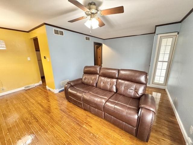 living area with ornamental molding, wood finished floors, a ceiling fan, and baseboards