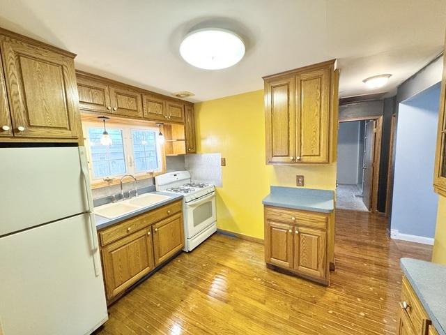 kitchen with white appliances, a sink, wood finished floors, and brown cabinets