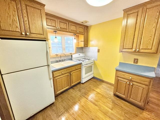 kitchen with white appliances, a sink, light wood-style floors, brown cabinets, and light countertops