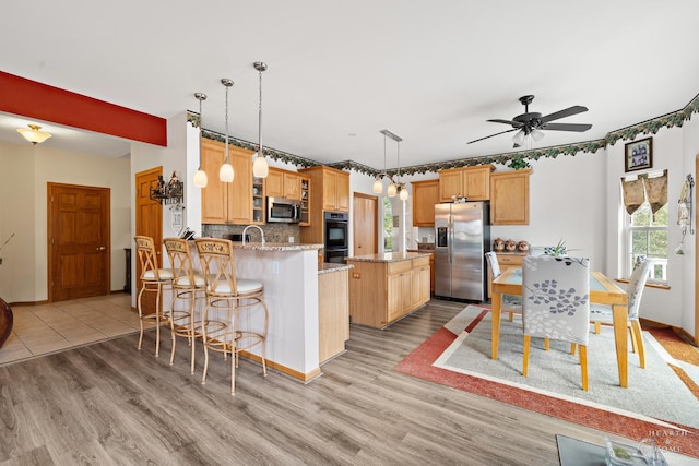 5008 Country Springs Dr, Johnsburg, IL 60051 - kitchen featuring appliances with stainless steel finishes, light wood finished floors, a peninsula, backsplash, and light stone counters