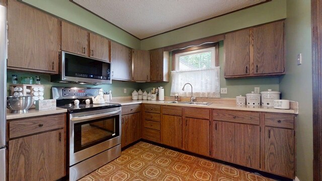 2702 Worcester Dr, Champaign, IL 61821 - kitchen featuring stainless steel appliances, a sink, light countertops, a textured ceiling, and brown cabinets