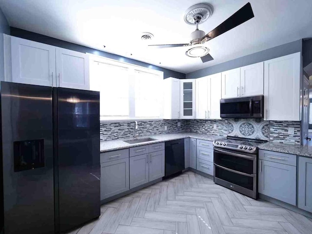 kitchen featuring black appliances, a sink, ceiling fan, decorative backsplash, and light stone countertops