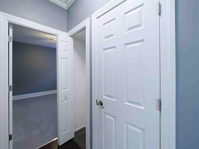 hallway with dark colored carpet, baseboards, and ornamental molding